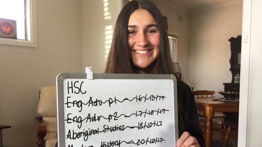 Rosa-May holds a white board on which she's kept track of all the HSC exams