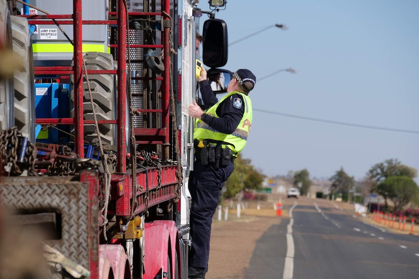 A police officer hanging off the side of a road train, breath-testing the driver.