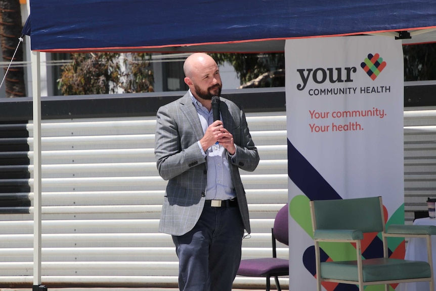 A man speak on a microphone in front of an outside crowd