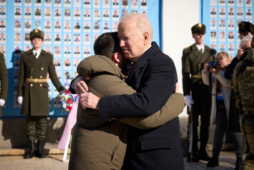 Two men hug as guards can be seen standing guard in the background. 