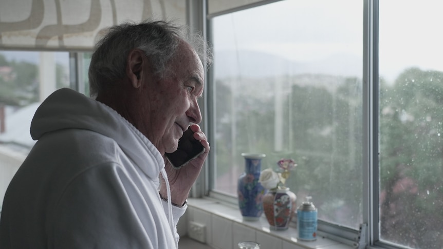 A man stands talking on the phone looking out the window.