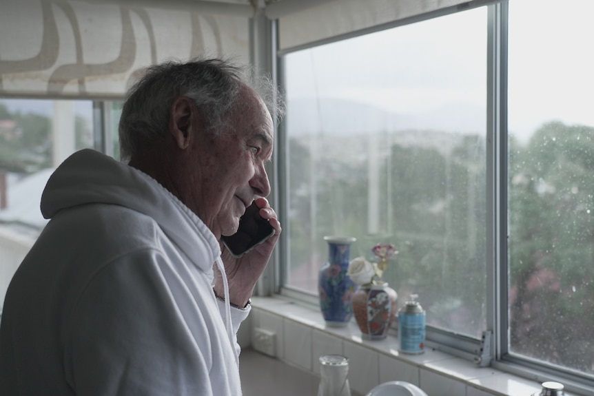 A man stands talking on the phone looking out the window.
