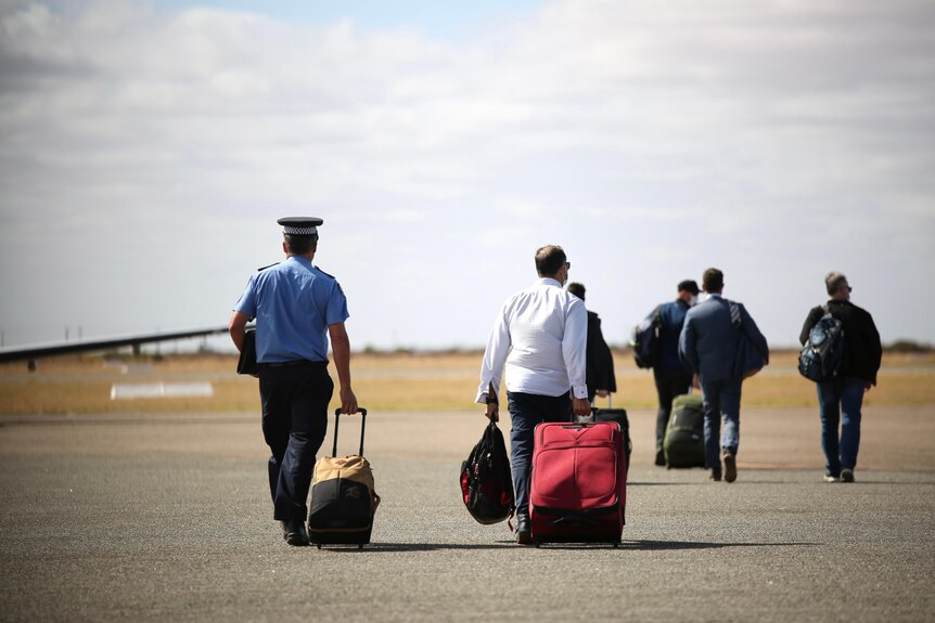 Police officers carry their suitcases to a waiting aircraft.