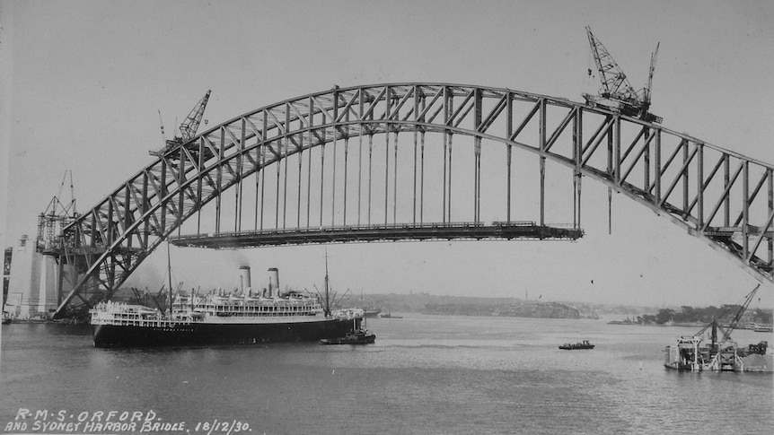 A black and white photo of the bridge with two cranes on it. 