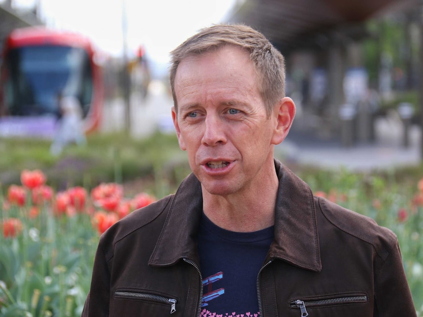 Shane Rattenbury speaks to the media in front of a light rail stop.