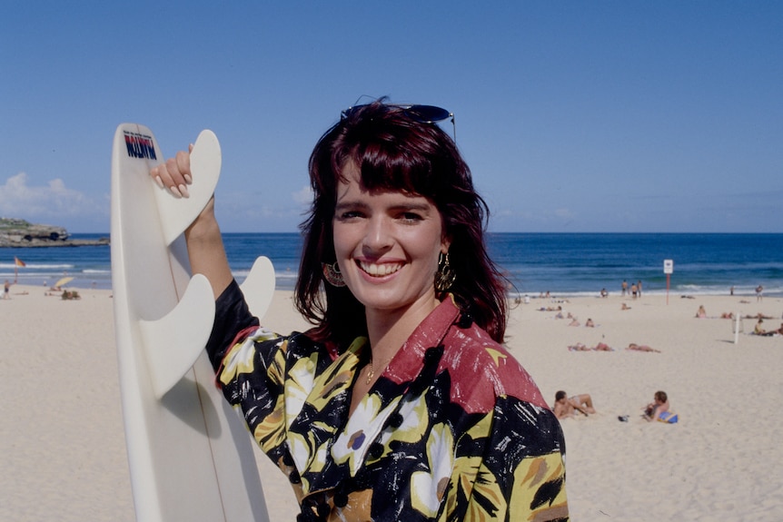 Woman at a beach holding a surfboard.