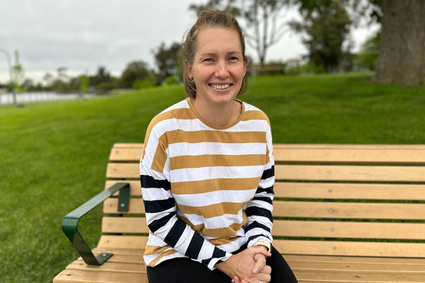 A woman wearing a brown and white striped top sitting on a park bench.