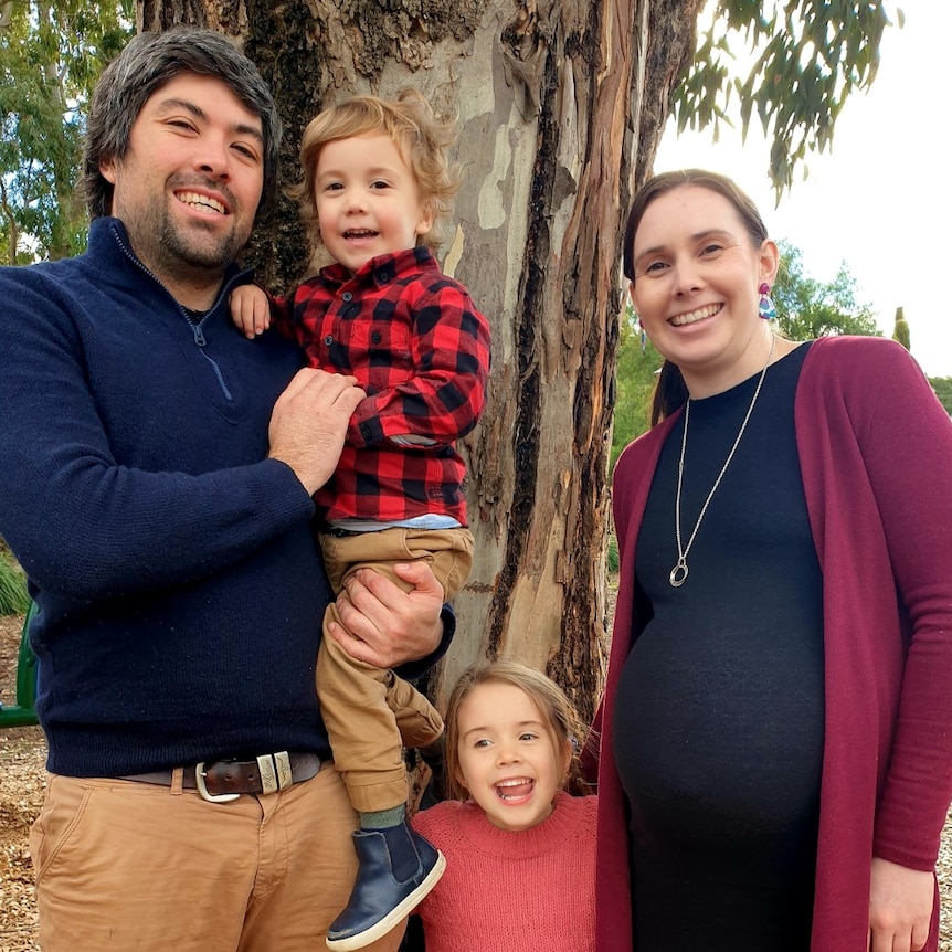 Smiling family with two parents and two kids posing outdoors.