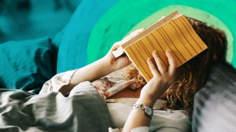Women in bed with book over her face for story on whether you are too sick to go to work