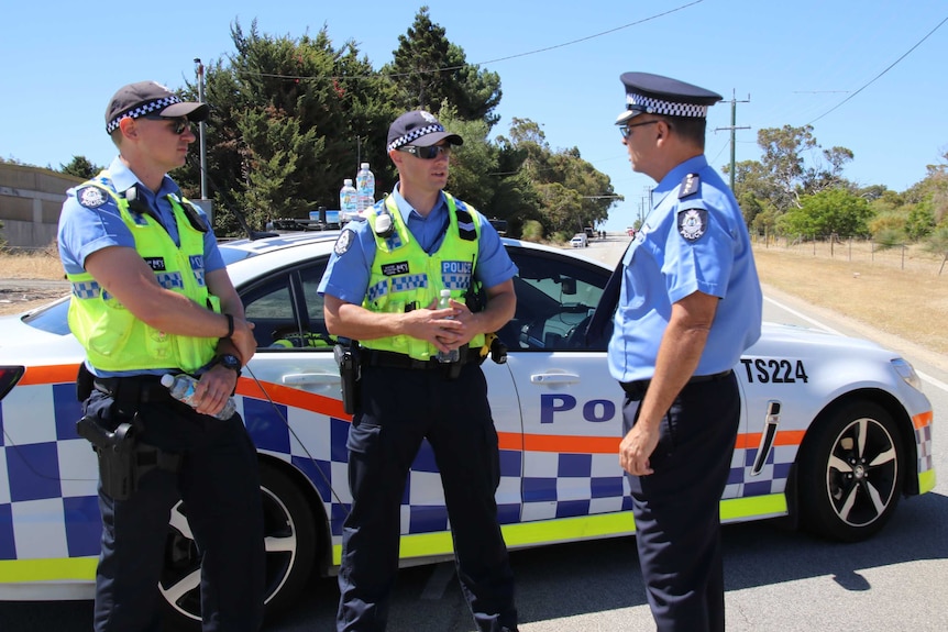 Three WA Police officers in uniform stand talking on a road in Munster in Perth in front of a patrol car.