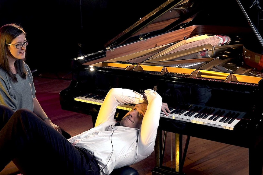 Simon Tedeschi playing the piano while lying on his back on the piano stool with his hands behind his head. It's for science.