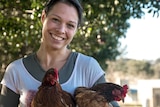 A lady stands holding some chickens.