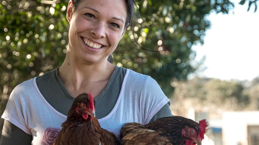 A lady stands holding some chickens.