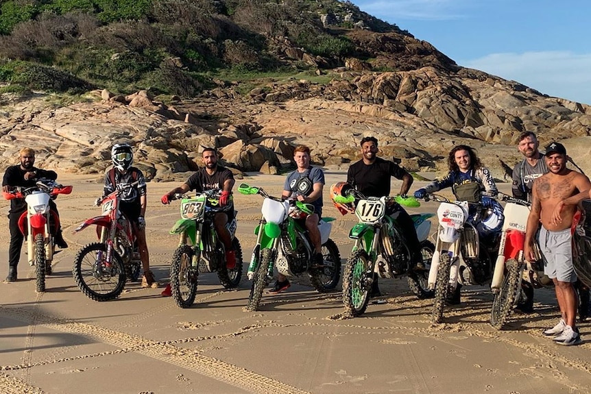 Eight guys on dirt bikes smile at the camera