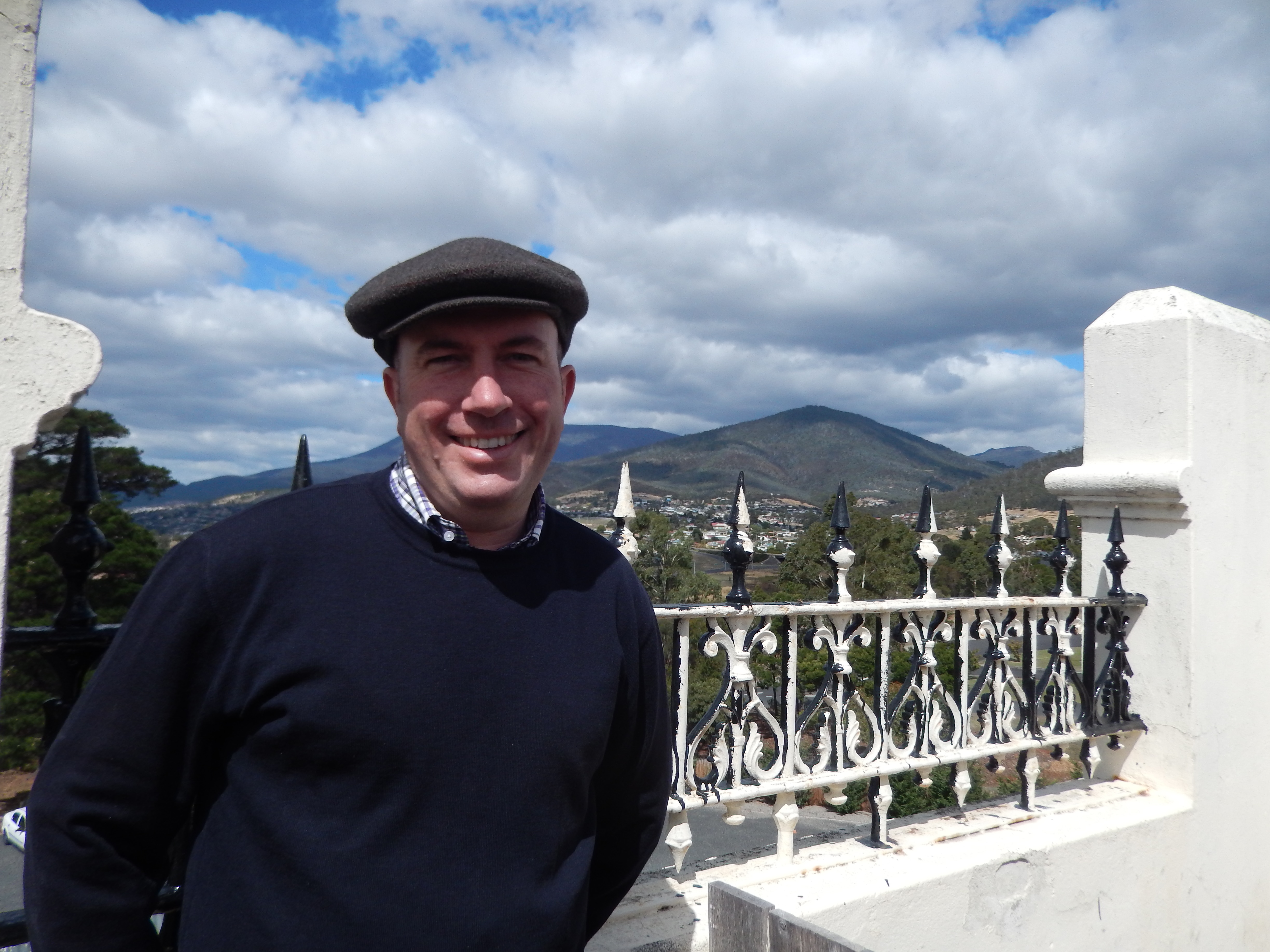 A man stands on the roof of a building, with mountains in the background.