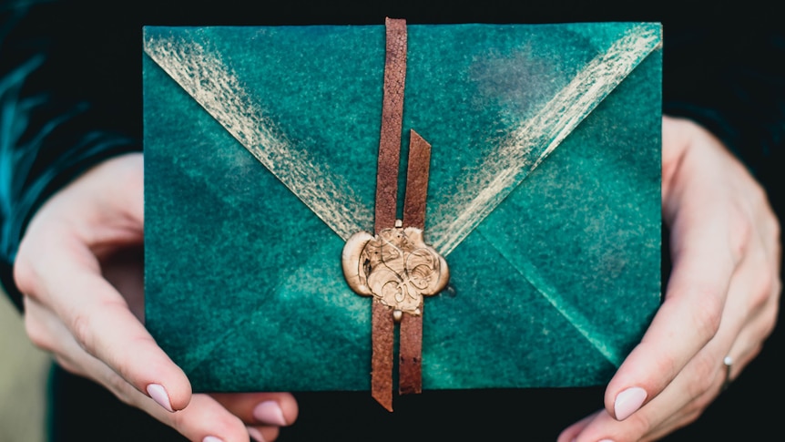 a close up of some hands passing the viewer an ornate envelope