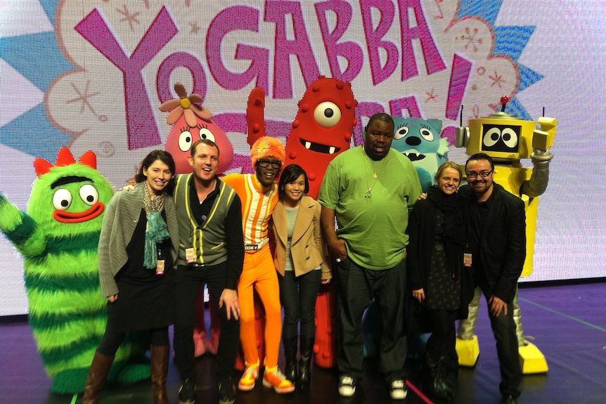 A group of adults and dressed up children's entertainment characters hugging and smiling at camera.