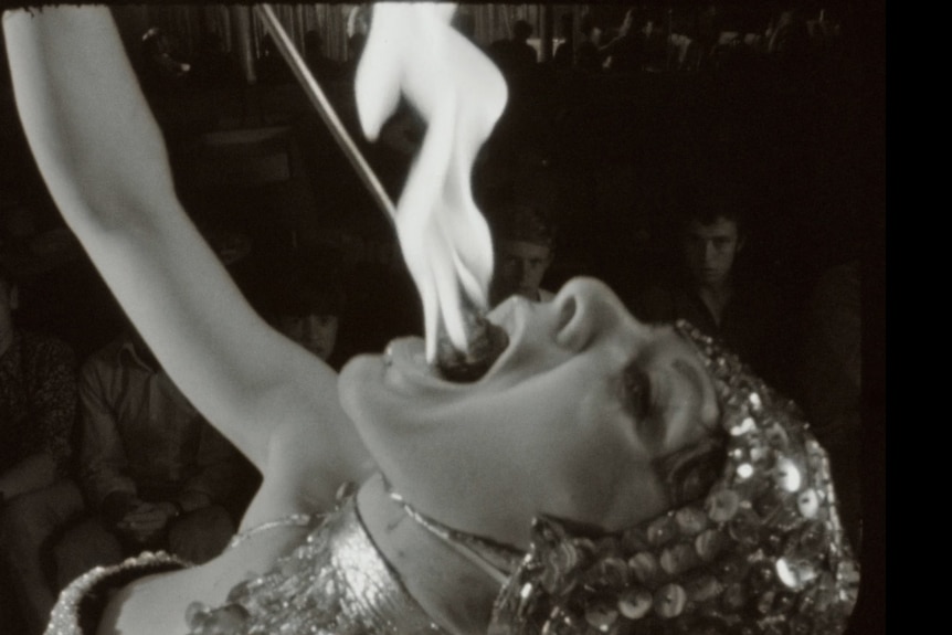 Close up on a fire-eating woman in a sparkly costume lowering a flaming torch into her mouth.