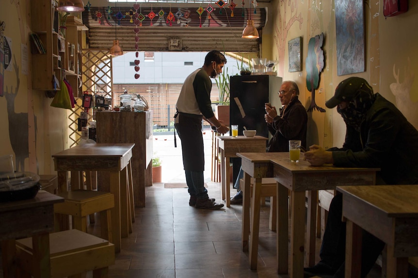 Two people sit at wooden tables inside a restaurant with coloured murals