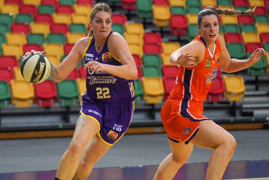 A Melbourne Boomers WNBL player dribbles the ball while being defended against by a Flames opponent.