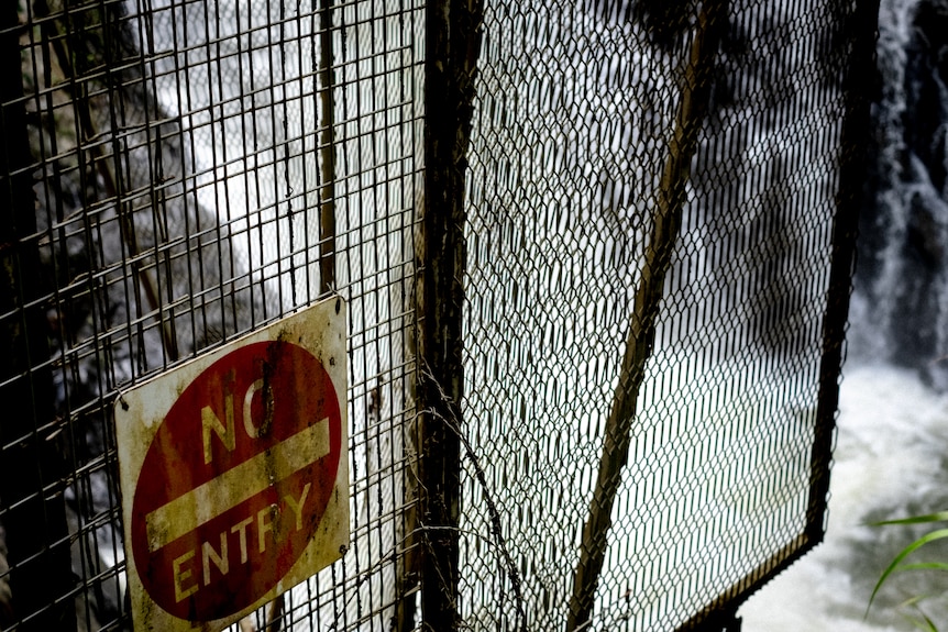 A 'No Entry' sign on a fence above a waterfall.