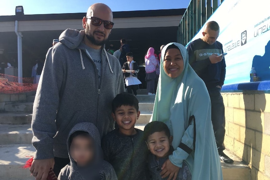 A photo family, parents and three kids outside a building.