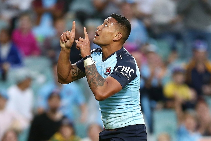 Israel Folau points to the sky with both hands and looks up in a blue rugby shirt