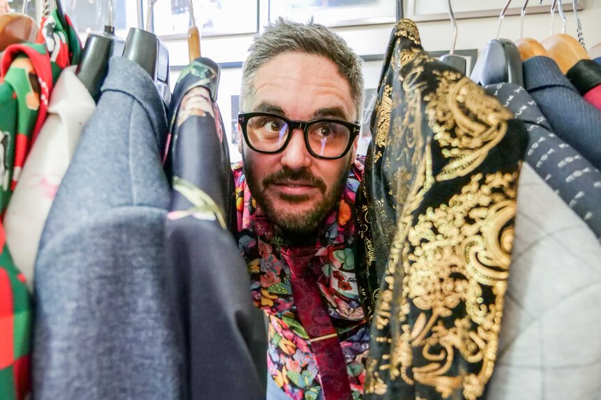 A man wearing glasses pokes his head between a rack of colourful jackets