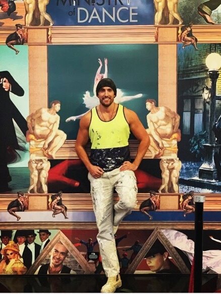A man stands wearing a hi-vis singlet leaning on a dance backdrop