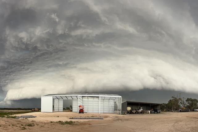 A photo of a huge storm cloud approaching a shed in an isolated outback setting.