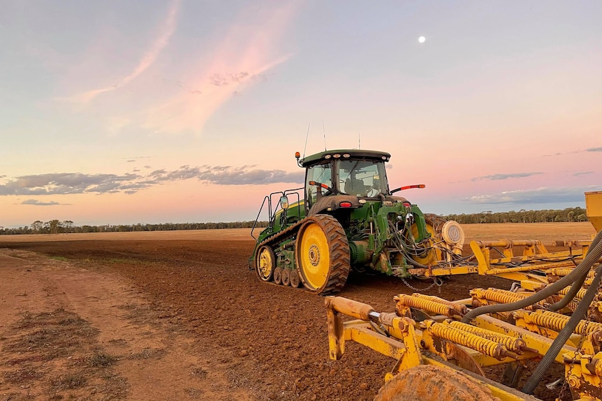A large green tractor ploughs a field at dusk