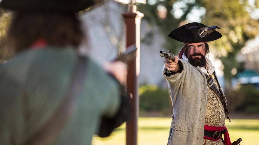 Two men is historic dress point pistols at each other mid-duel.