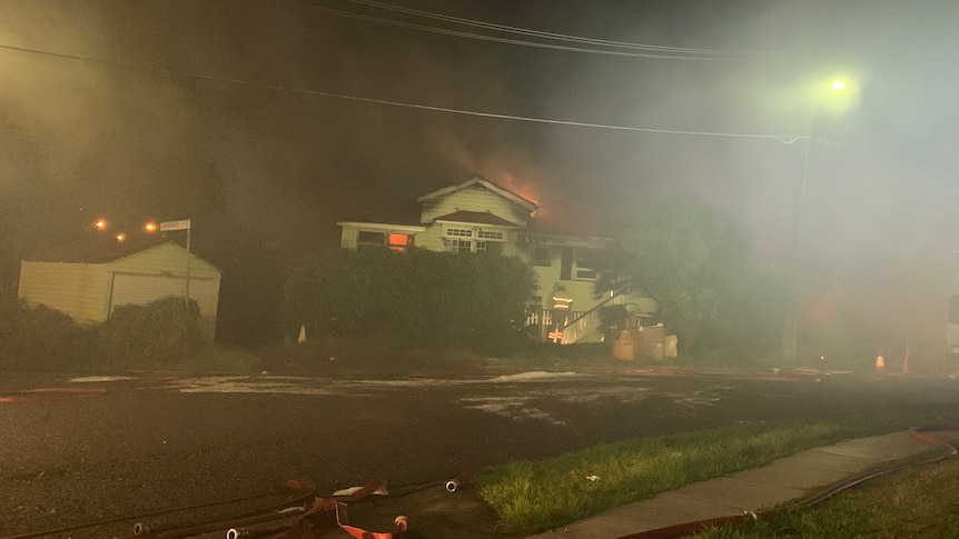 Flames billowing over the roof of a Queenslander, smoke fills sky