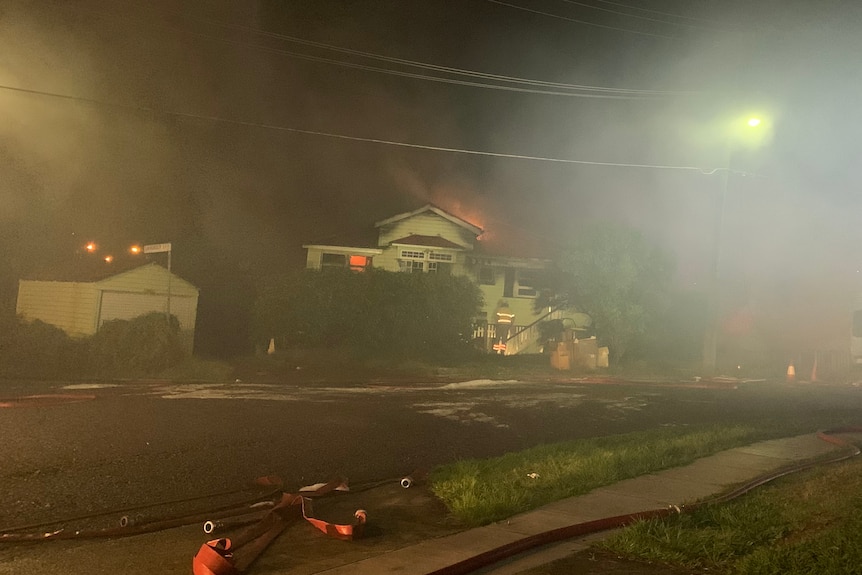 Flames billowing over the roof of a Queenslander, smoke fills sky