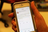 A hand holds an iPhone displaying a tweet from Queensland Fire and Emergency