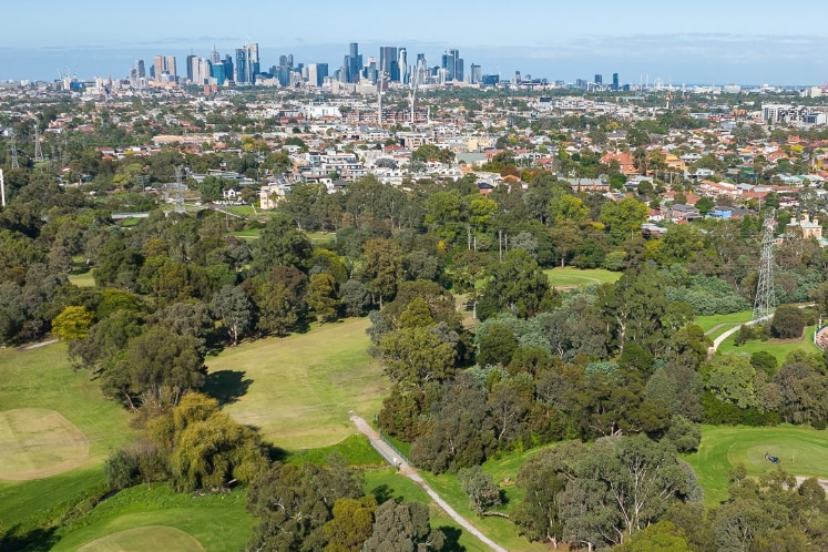 An aerial view of a golf course, with the city on the horizon.