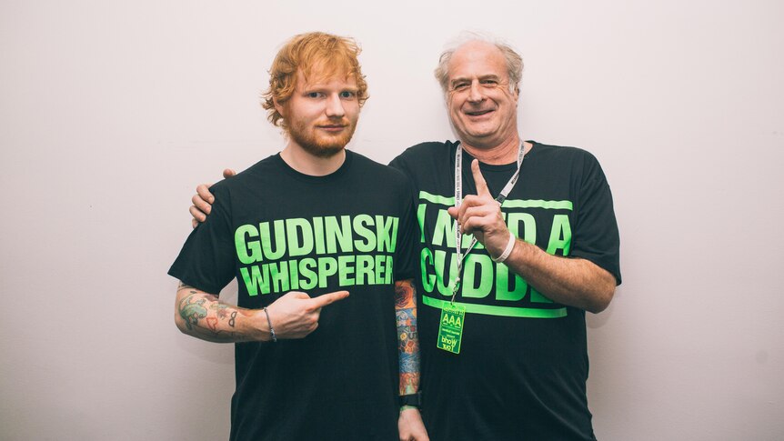 Ed Sheeran points at Michael Gudinski who hugs him and points a finger up. They wear matching black t shirts