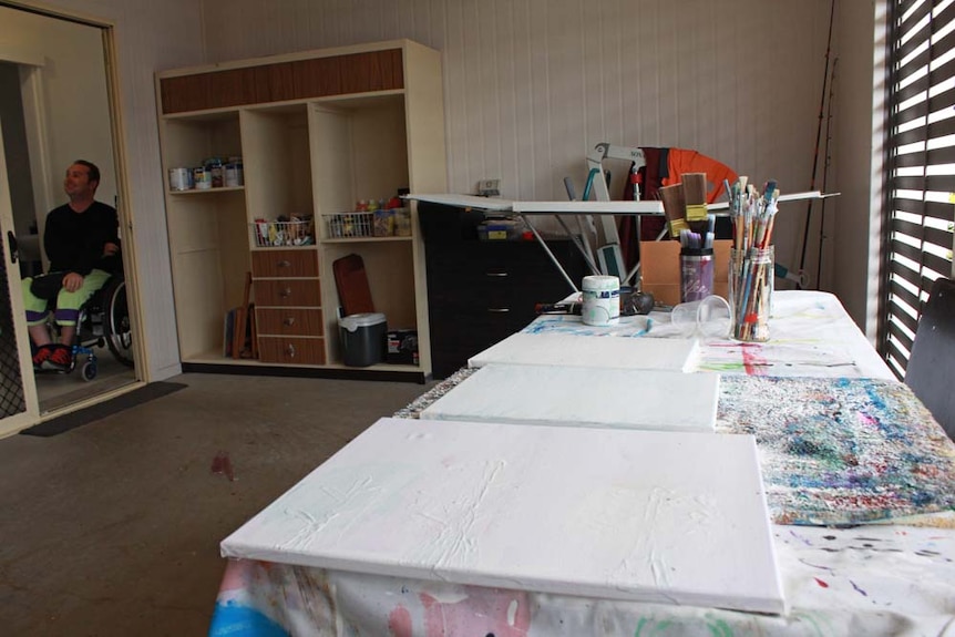 Three white canvases on a table in the garage. David can be seen from the hallway through door.