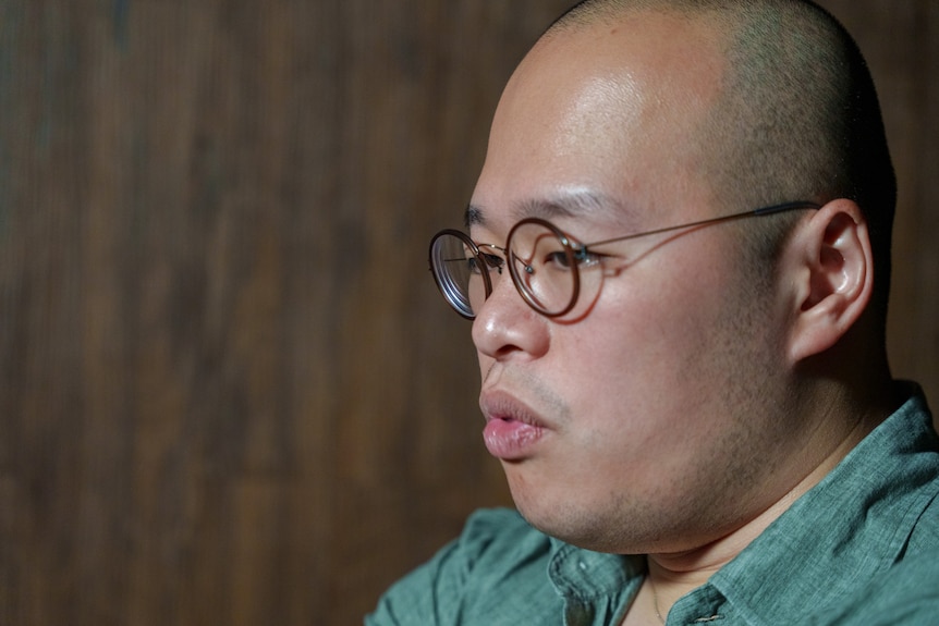 A close up of a bald man wearing glasses as he speaks.