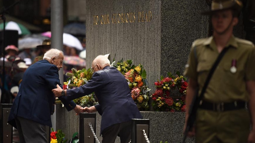 Two elderly men help each other during the Remembrance Day service at the Cenotaph in Martin Place.