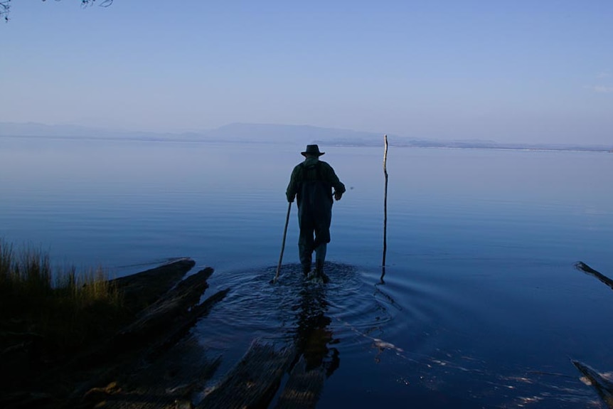 A man in silhouette walking on the submerged slips at Sarah Island by the early light of dawn.