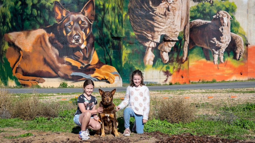 Two children with a dog in front of a silo.