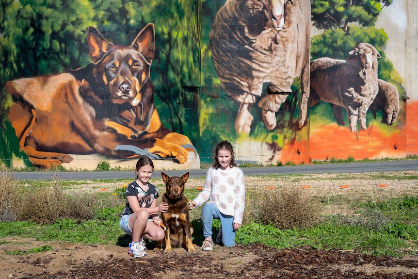 Two children with a dog in front of a silo.