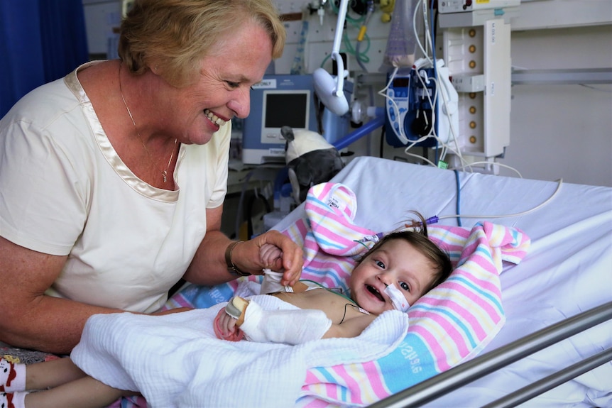 A sick infant in bed with a woman looking over her. Both are laughing.