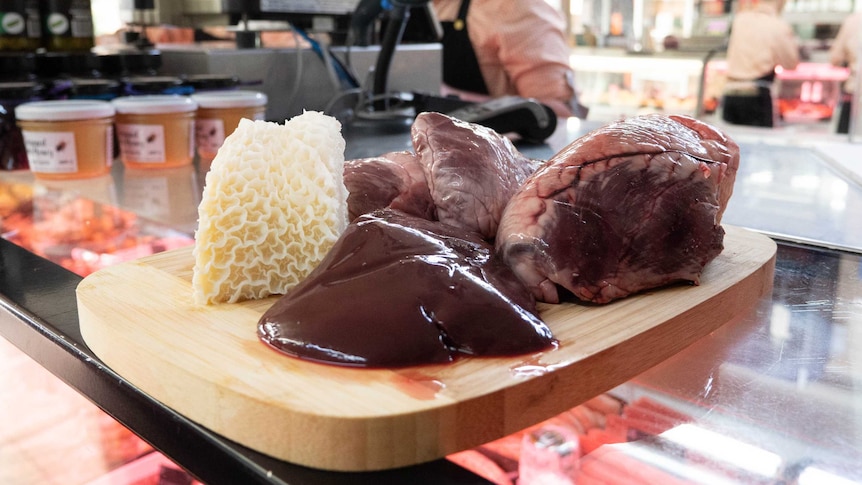 Different kinds of offal on a wooden board, sits on a glass countertop at butcher.