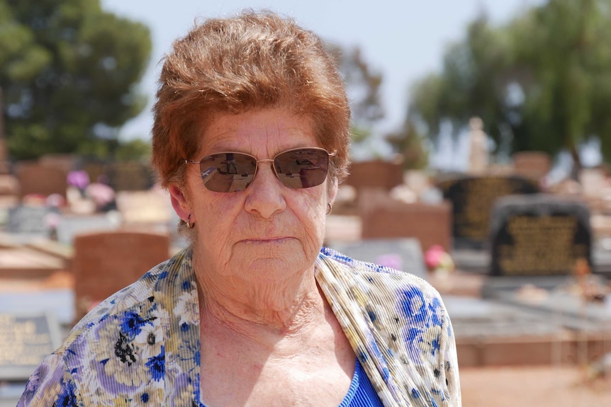 A lady with a blue top stands in a cemetery.