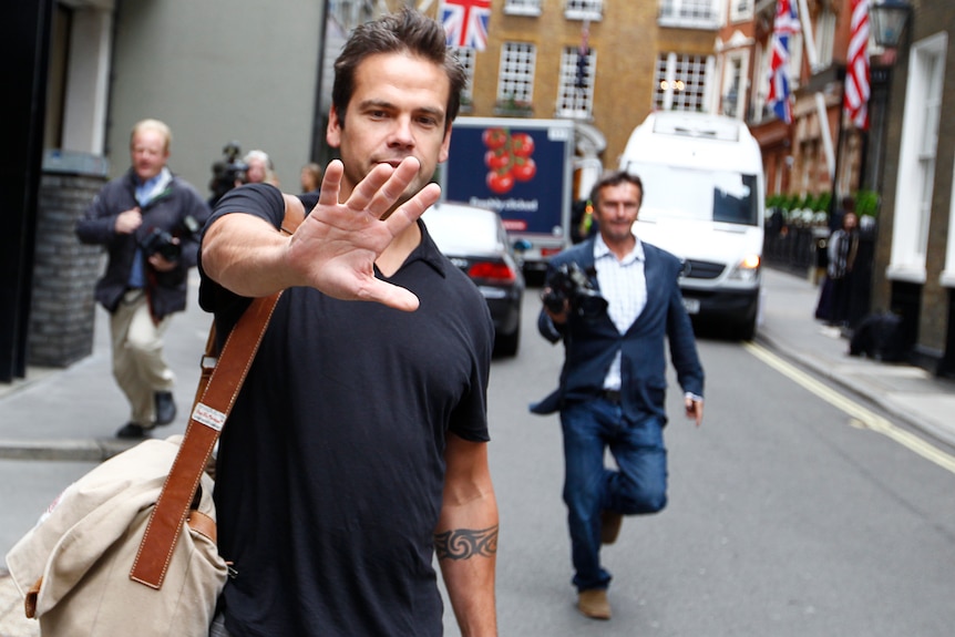 Lachlan in blue polo on London Street puts his hand out to block the camera, union flag bunting in background