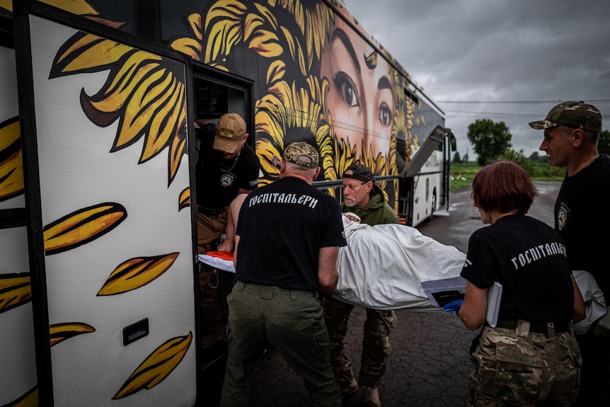 A group of medics in black shirts load a man on a stretcher onto the bus.