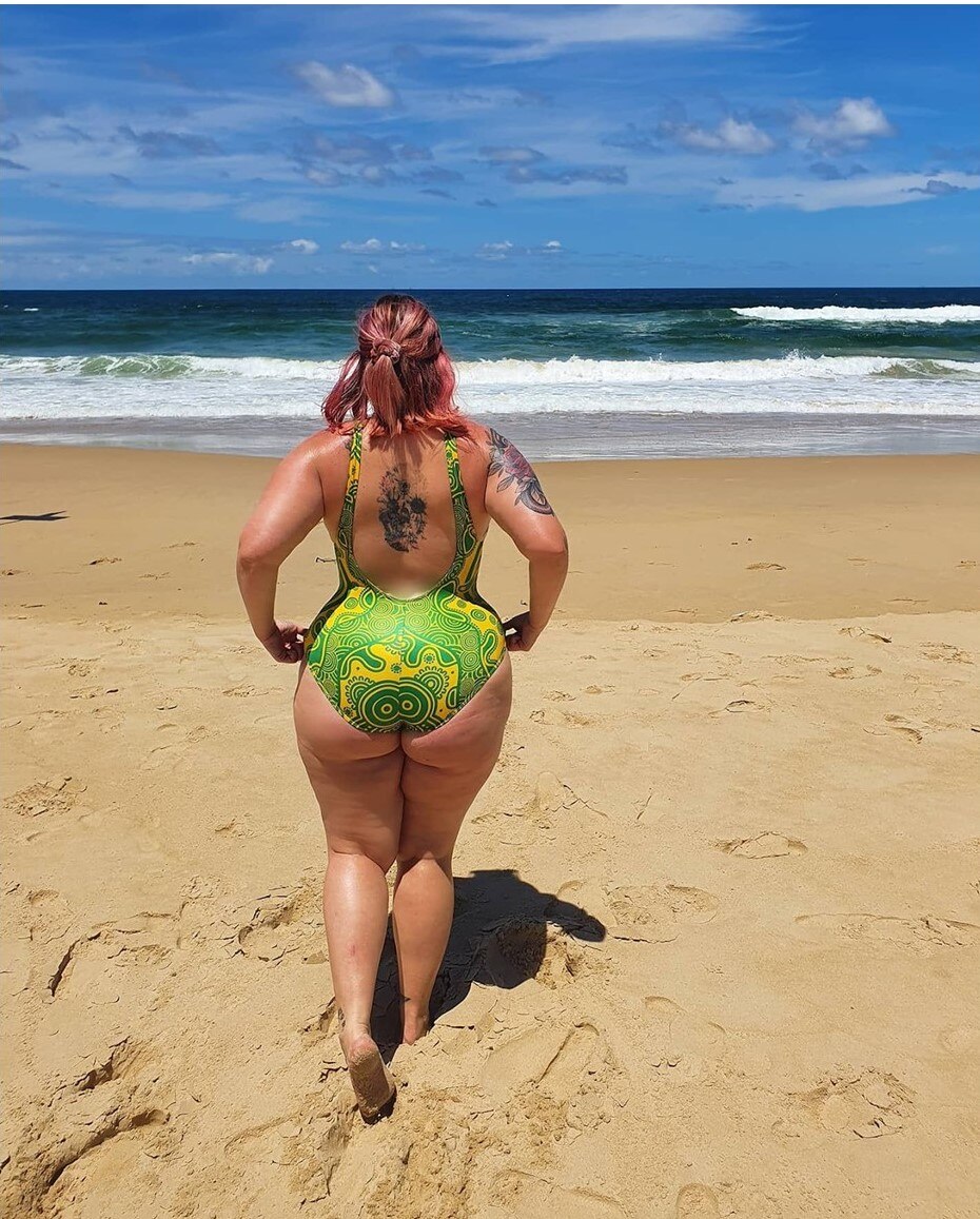Photo of the back of a woman wearing a bright green swimsuit. She is affected by lipoedema around her hips and legs