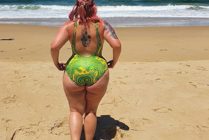 Photo of the back of a woman wearing a bright green swimsuit. She is affected by lipoedema around her hips and legs